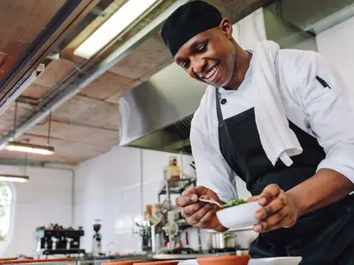 Happy male cook wearing apron standing by kitchen counter preparing food.