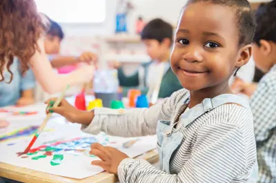 Little girl at daycare smiling at camera while doing crafts