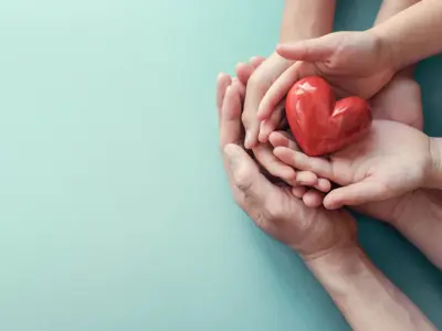 Adult and child hands holding red heart on aqua background concept for health