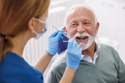 Dental hygienist checking the teeth of a smiling elderly man in a dental office.