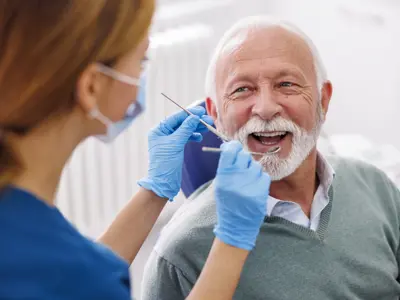 Dental hygienist checking the teeth of a smiling elderly man in a dental office.