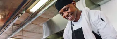 Happy male cook wearing apron standing by kitchen counter preparing food.