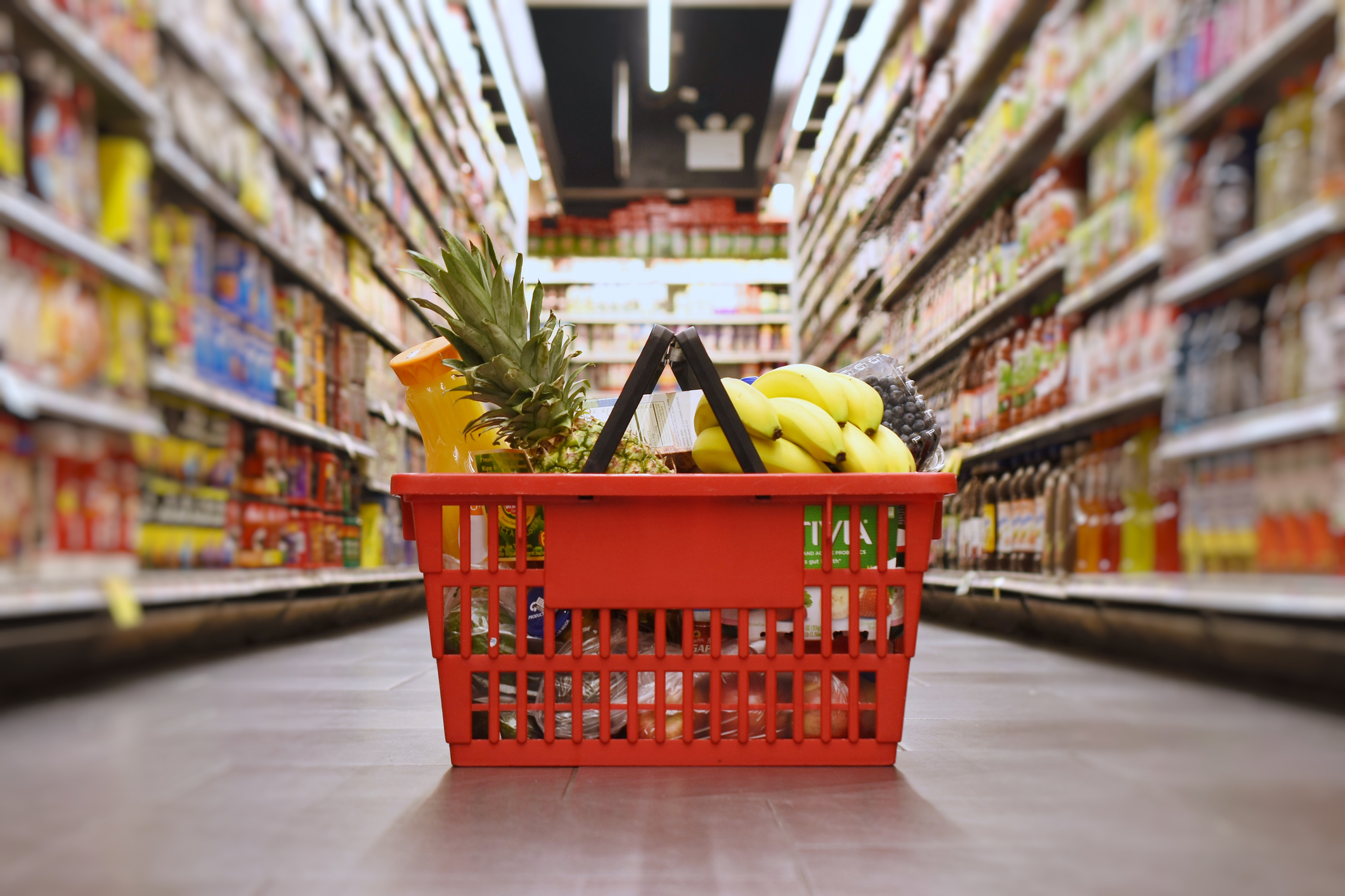 Full grocery basket sitting on the floor in the middle of a isle in a grocery store.