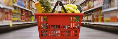Full grocery basket sitting on the floor in the middle of a isle in a grocery store.