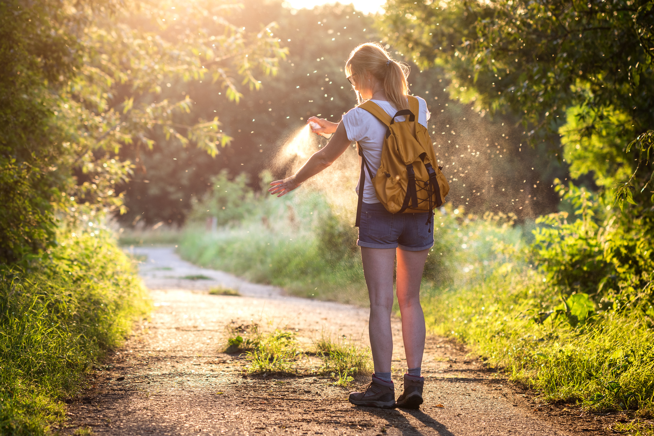 Woman with backpack applying insect repellent agains mosquito and tick outdoors.